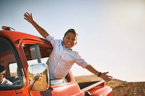 Take on life with open arms. a young cheerful boy leaning out of a red pickup truck with his arms stretched out while looking into the camera