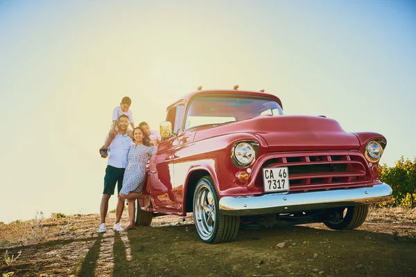 Going for a ride with the family. a cheerful family posing for a portrait together outside next to a red pickup truck