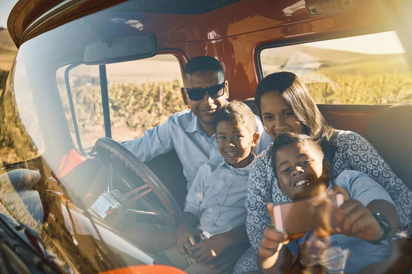 Our family are stuck together like glue. a cheerful young family driving in a red pickup truck on a rural road while taking a self portrait on a cellphone together