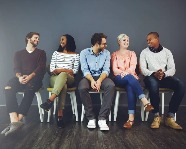 We can learn lots by just talking to each other. Studio shot of a group of young people waiting in line on chairs and chatting against a gray background