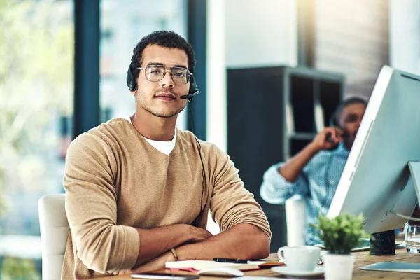 I want to help in every way I can. a call center agent sitting at his desk with his colleague blurred in the background