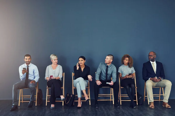 Next in line for a new job. Studio shot of a group of businesspeople using wireless devices while waiting in line