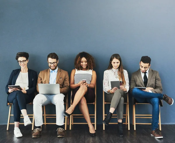 Online entertainment is how they handle their pre-interview nerves. Studio shot of a group of businesspeople using wireless technology while waiting in line against a gray background