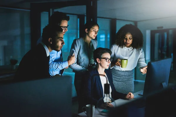 Giving their best under pressure. colleagues standing together as they work on something on a computer at night