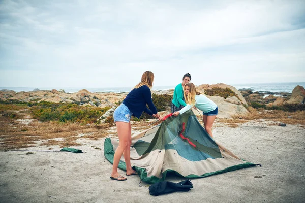 We all pitch in to set up the tent. a group of female friends setting up a tent outdoors