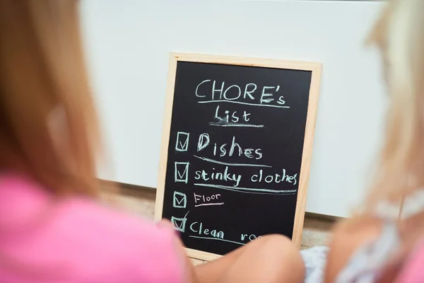 Time for chores. Rearview shot of two little girls looking at a list of chores on a chalkboard at home