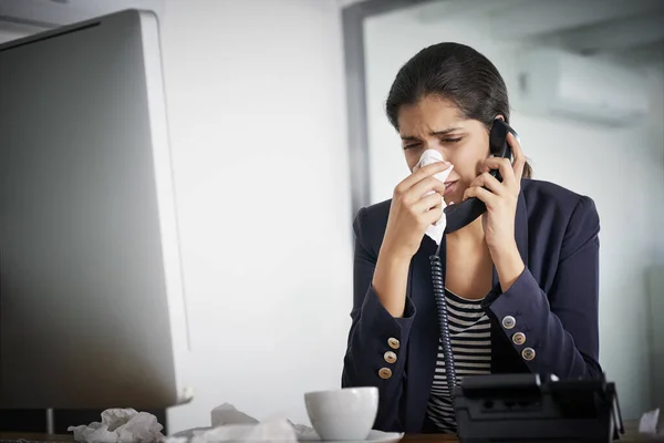 Keep strong and beat this cold. a young businesswoman making a call while blowing her nose and working in the office