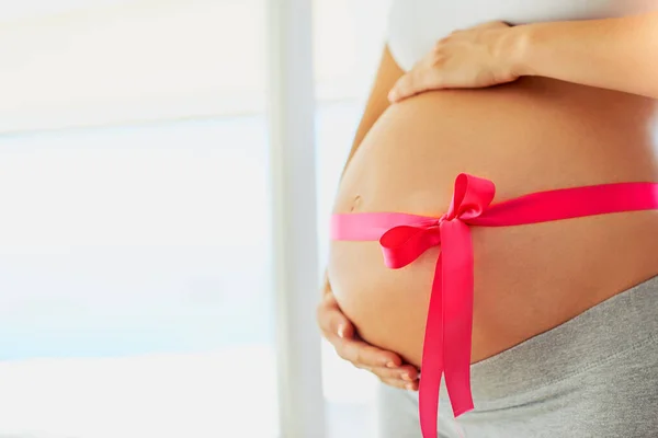 Lady in waitingfor her little princess. a pregnant woman with a pink ribbon tied around her belly