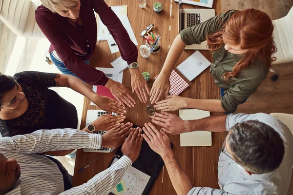All hands on deck to get things done. High angle shot of a group of colleagues joining their hands in solidarity during a meeting in a modern office