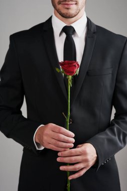 You as beautiful as a rose. Studio shot of a well-dressed man holding a red rose against a gray background