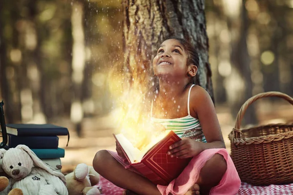 Books open up bright new worlds. a little girl reading a book with glowing pages in the woods