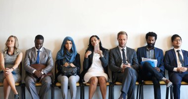 Each candidate has something different to offer. a group of well-dressed businesspeople seated in line while waiting to be interviewed