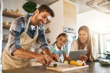 There are so many exciting recipes to try online. two happy parents and their young daughter trying a new recipe in the kitchen together