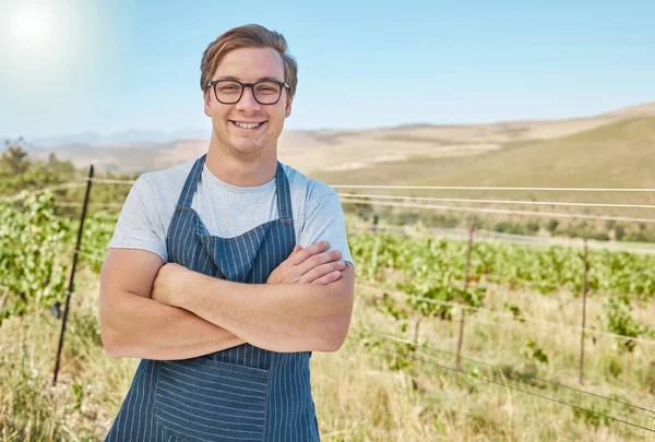 Vineyard and happy farmer man in the countryside with smile at a farm in nature in summer. Health, agriculture and success portrait of a young worker on a field in sustainability on a sunny day