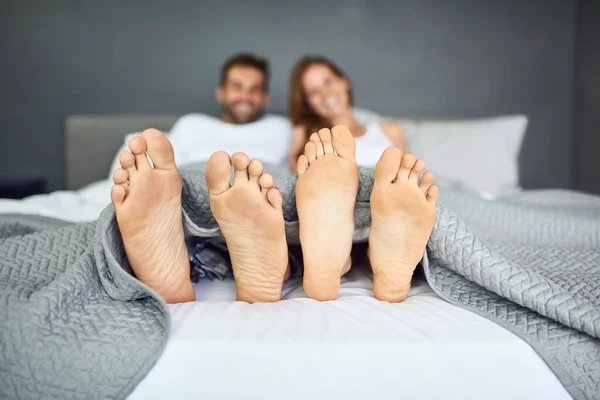 Sunday is bed day. a happy young couple relaxing in bed with their feet poking out from under the bed sheets