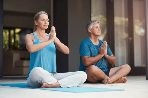 Peaceful minds are happy minds. a mature couple peacefully engaging in a yoga pose with legs crossed and hands put together