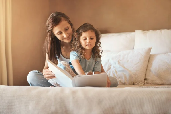 Please read it again mommy. a happy mother and daughter at home reading a storybook on the bed