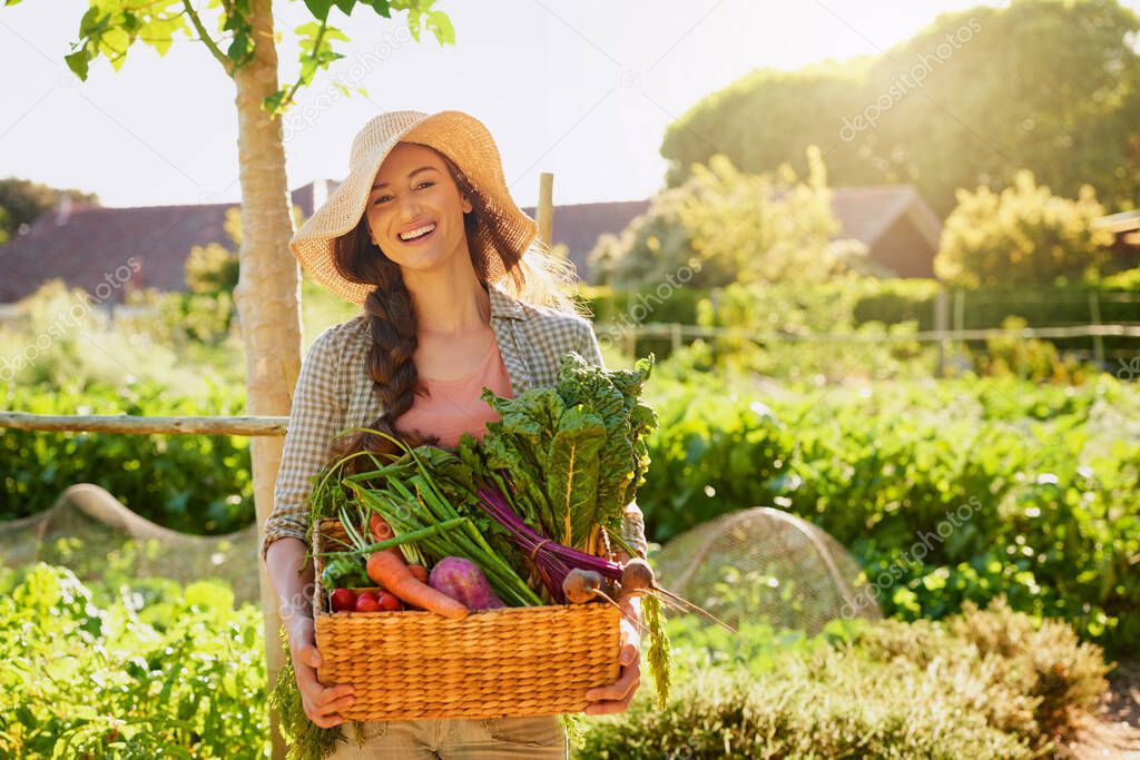 Grown by Mother Nature herself. Portrait of a young woman carrying a basket of freshly picked produce in a garden