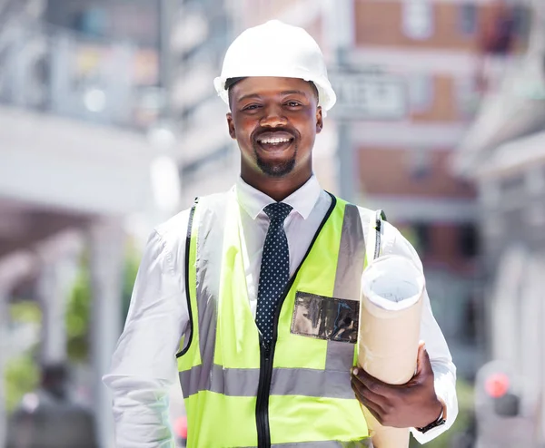Business, builder and contractor man holding building plans with a vision for success in construction. Portrait of a happy smiling black man with a plan and idea for architecture design in the city