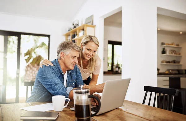 Couple with laptop planning finance, banking and checking retirement budget while becoming debt free at home. Smiling, happy and cheerful mature man showing woman an approved bank loan on technology.