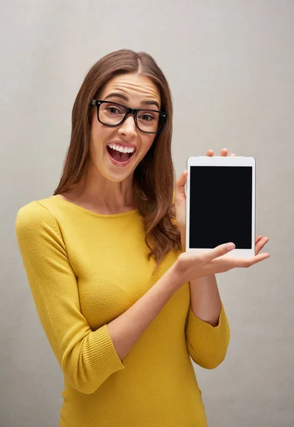 Its a game changer. Studio portrait of an attractive young woman posing with her tablet against a grey background