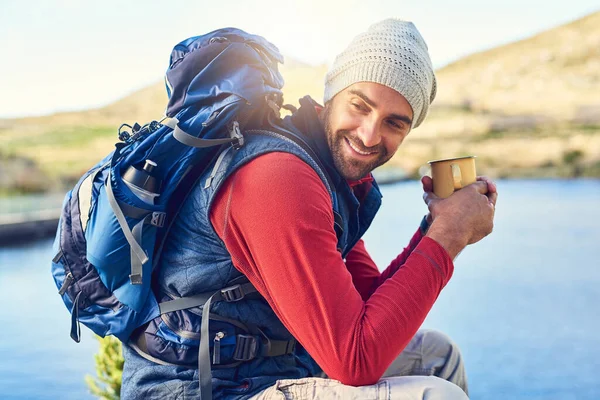 Getting his caffeine fix in the great outdoors. a happy hiker drinking coffee while admiring a lake view on a trail