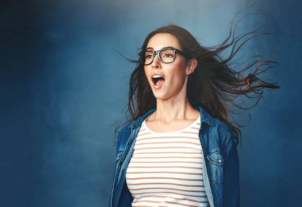 The surround sound effect. Studio shot of a young woman with air being blown in her face against a blue background