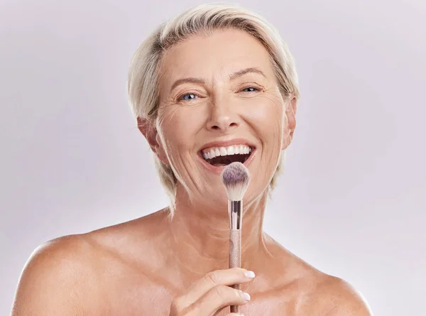 Beauty, makeup skincare with a senior model holding a blusher brush in studio against a gray background. Portrait of an elderly woman with a smile posing for wellness, healthcare and cosmetics.