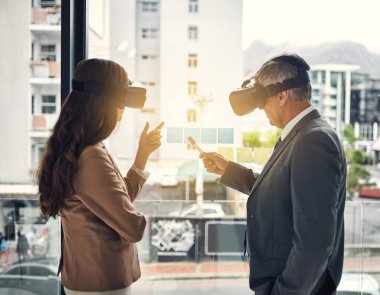 There are many ways to perceive success. two businesspeople wearing VR headsets while working with notes on a glass wall in an office