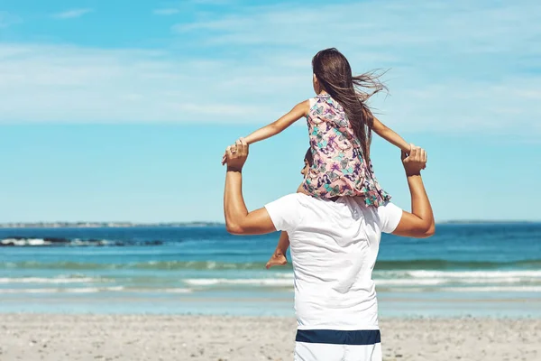 Getting a better view on daddys shoulders. Rearview shot of a young father and his daughter enjoying a day at the beach