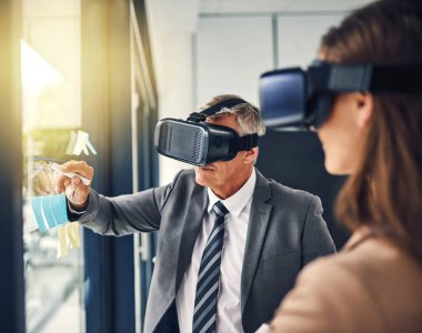 Reaching out to where it was thought impossible before. two businesspeople wearing VR headsets while working with notes on a glass wall in an office