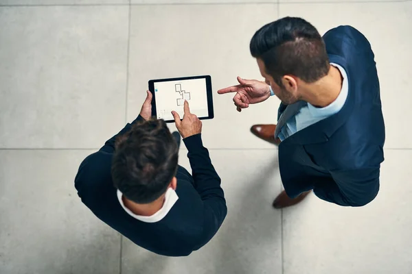 Its the device that helps to expand their ideas. High angle shot of two businessmen working together on a digital tablet in an office