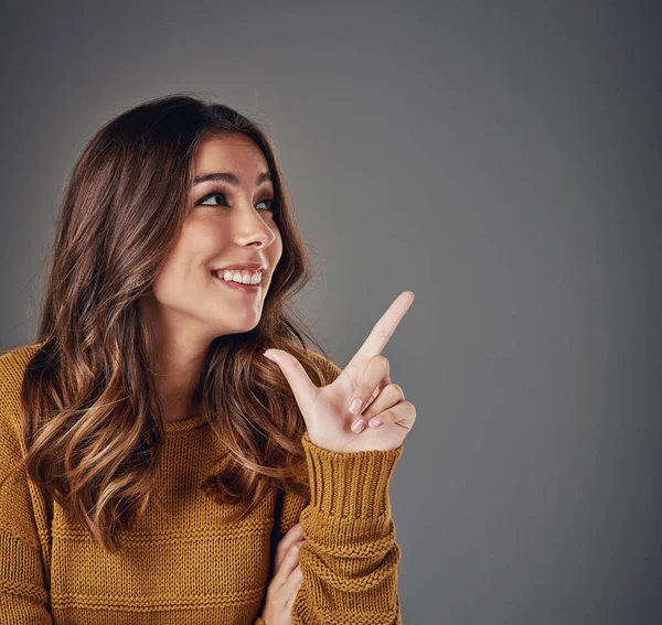 Would you look at that. an attractive young woman pointing to copyspace against a grey background