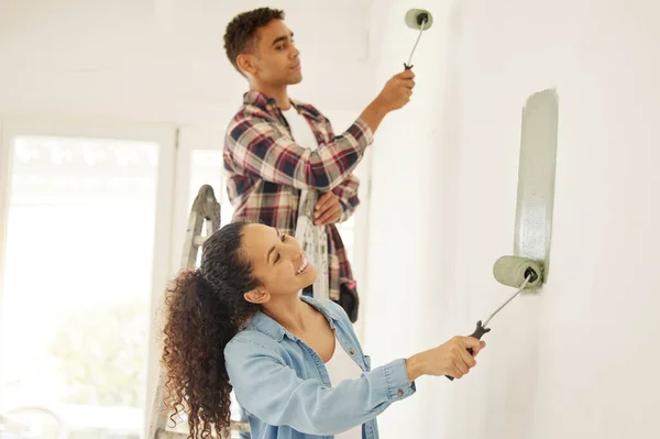 Painting, love and renovation with a couple doing DIY in a room for improvement and remodel of their home. Young man and woman working with green paint on a wall to renovate their domestic house.