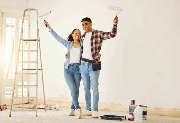 Portrait of happy couple painting the new living room in a home or apartment. Man and woman with paintbrush to decorate a wall color and renovation the house interior with smile or happiness together.