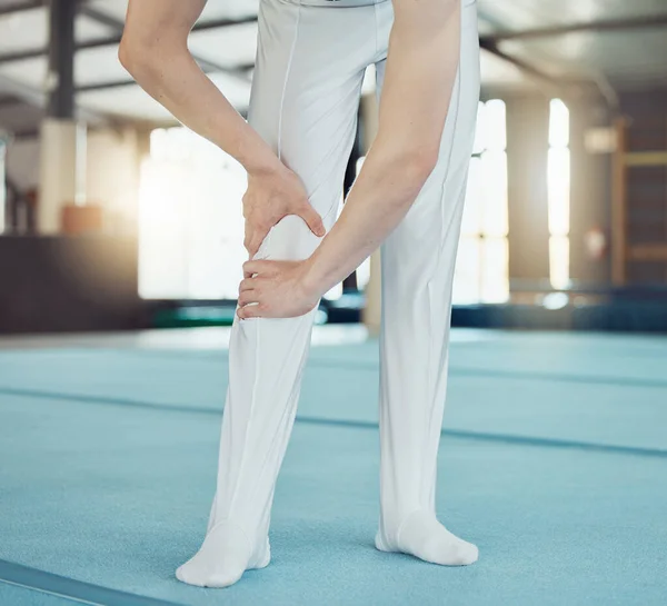 Gym, sport and injury of a professional gymnast suffering from leg pain or ache during training indoors. Sore knee, legs and muscle from intense athletic practice or workout exercise for competition