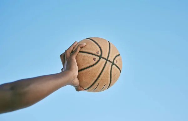 Basketball, active and sports man hand holding ball showing victory, power or athletic fitness from below with blue sky background. Player, black man or athlete arm practicing for professional league.