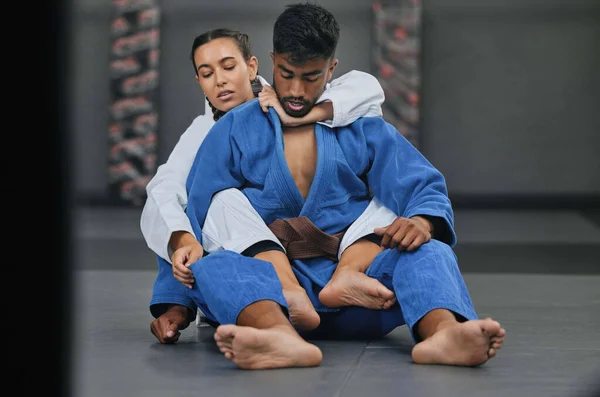 Woman in karate fitness training class with coach, learning self defence in gym class and fighting male trainer at fight club. Man teaching a student martial arts, foot control and rear naked choke.
