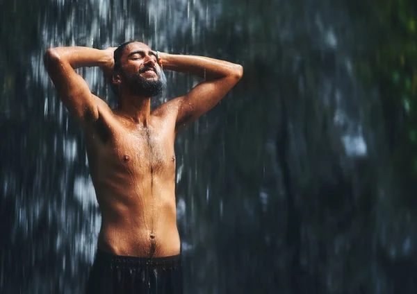 Who needs a shower at home if you have this. a young man standing under a waterfall being completely soaked in water but loving every moment of it