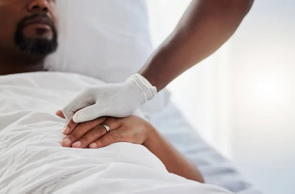 Cancer, death and medical support with a patient and nurse in a hospital for health, wellness and love. Closeup of the hand of a doctor giving comfort and care to a man lying in a clinic bed.