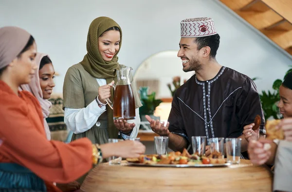 Group of muslim people celebrating Eid or Ramadan with iftar at home with food, drink and family. Young Islam woman pouring juice for a happy, smiling and positive man while breaking fast together.