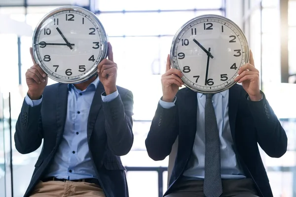 Times a wasting. two businessmen holding clocks over their faces in the office