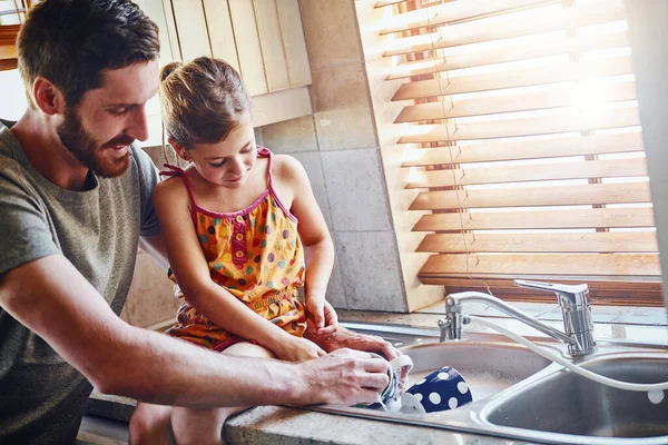 Chores are a part of their family routine. a father and his little daughter washing dishes together at home