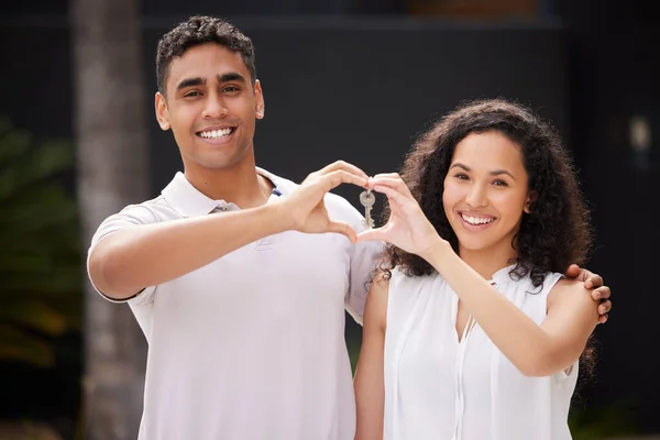 Happy couple buy real estate with key and heart hand sign and a smile together. Man and woman with keys or happiness with property rent or purchase of house, family home or apartment with love.