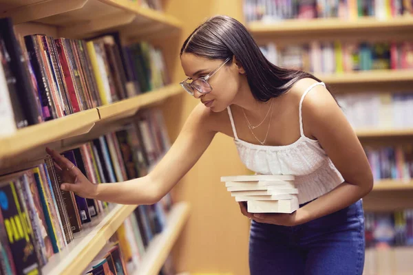 Library, books and woman reading print book for her college or university education and learning. Knowledge of young gen z scholarship student at shelf, studying for an English project exam or test.