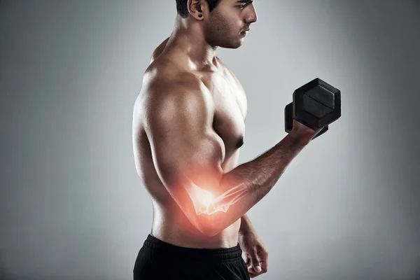 Pain and gain. a sporty young man working out with a dumbbell against a grey background