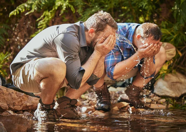 Hiking men splash water on face for calm, relax and cleaning dirt after trekking on rock or hike in countryside forest. Earth, freedom after camping in nature and travel along mountain river or lake.