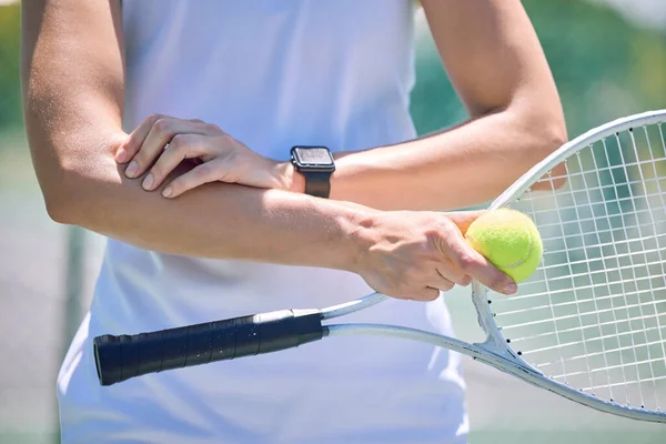 Sports, arm pain and tennis player with a racket and ball standing on a court during for a match. Closeup of a health, strong and professional athlete with equipment touching a medical elbow injury