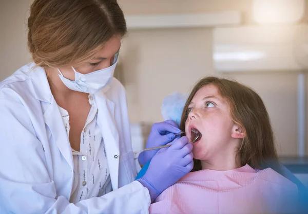 Checking for decay. a dentist examining a little girls teeth