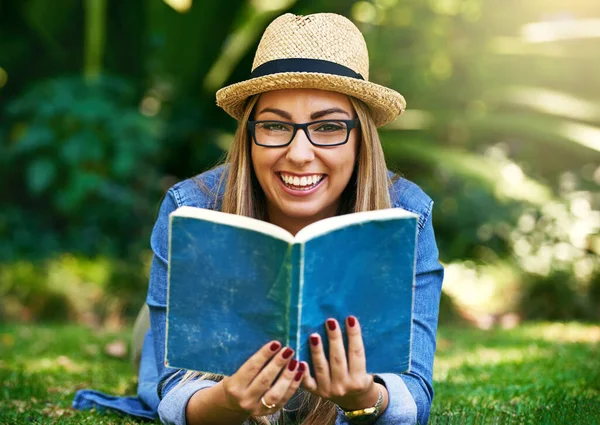 The outdoors is the best place to read. Portrait of an attractive young woman reading a book while lying outside on the grass